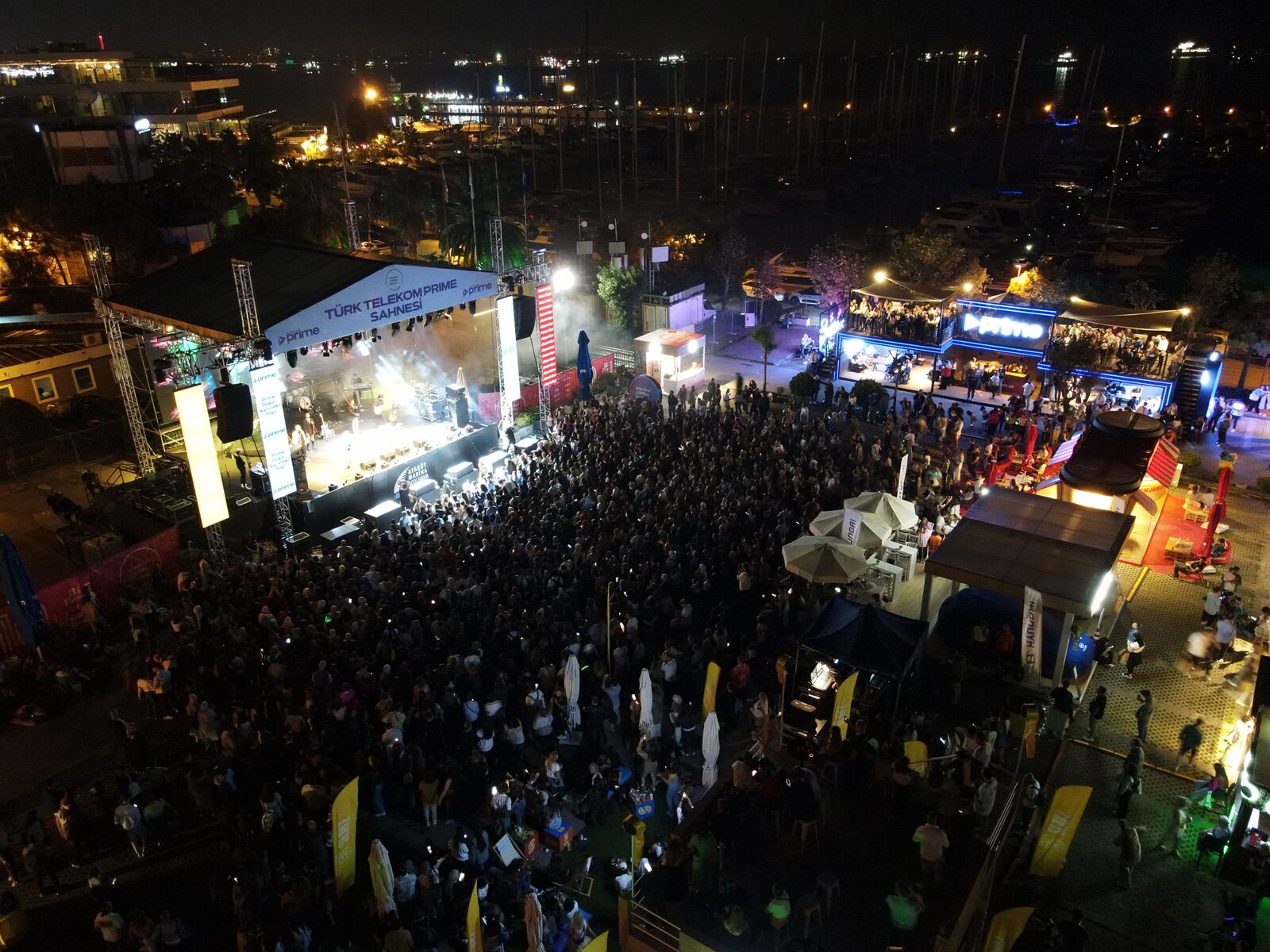 The festival site at night, a dense crowd between lit stands