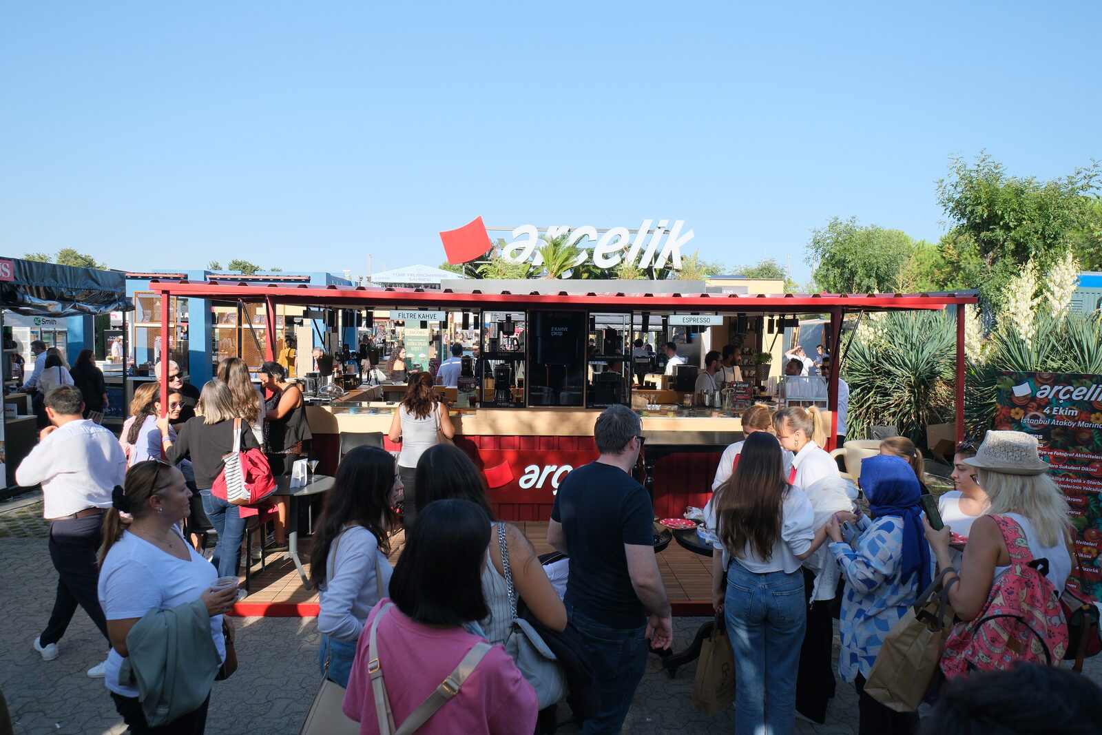 Visitors walking past a red-branded stand in bright daylight