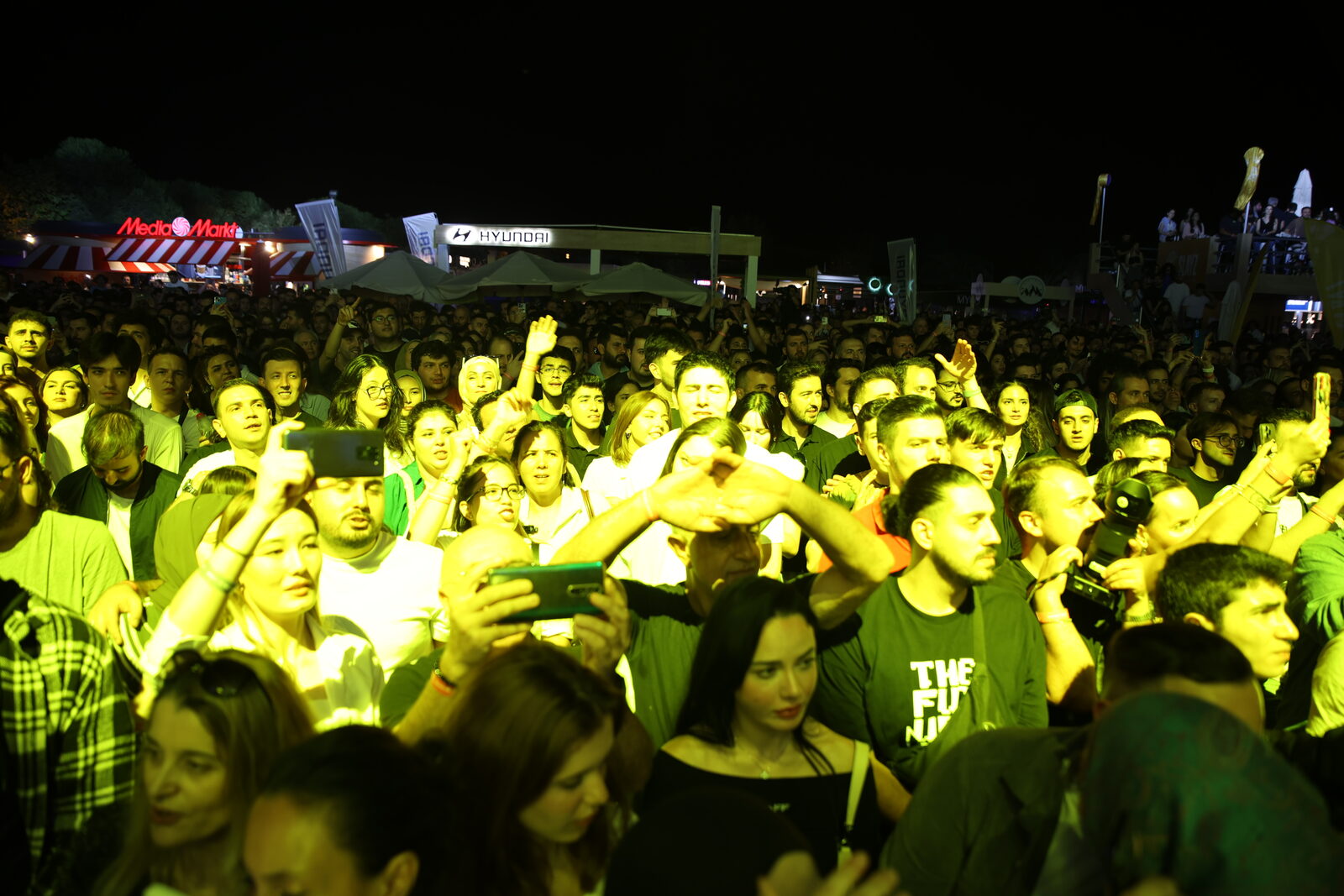 A night crowd under green stage light with arms raised