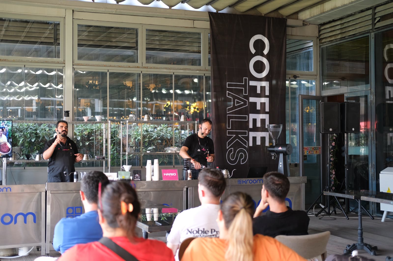Two speakers on the Coffee Talks stage in front of a seated audience