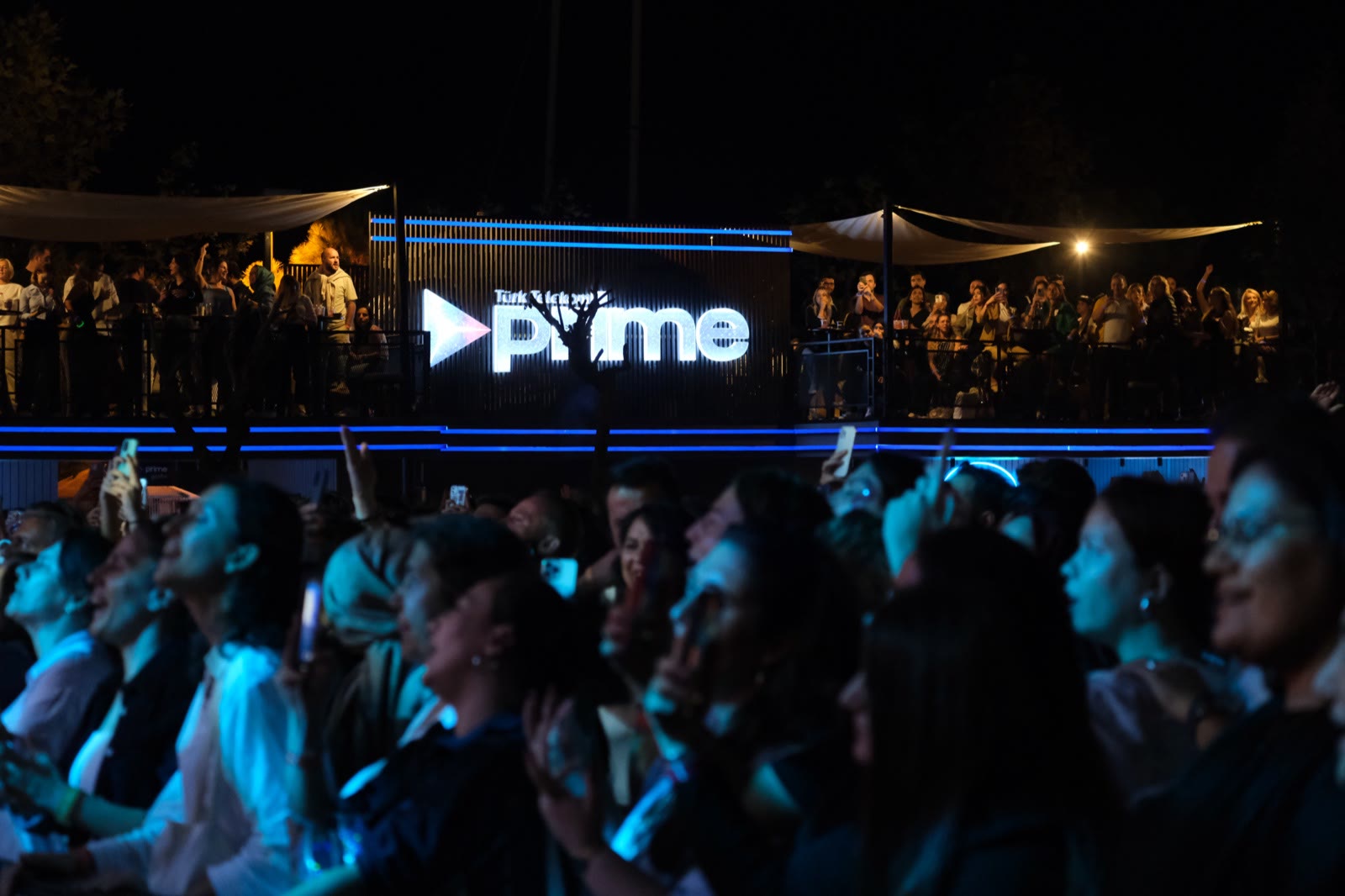 A cheering crowd at night in front of the lit stage lettering