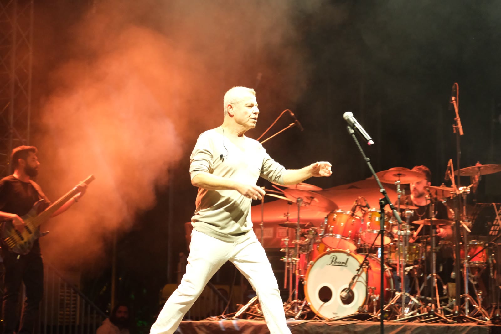 A singer mid-move on stage in red light, the drummer behind