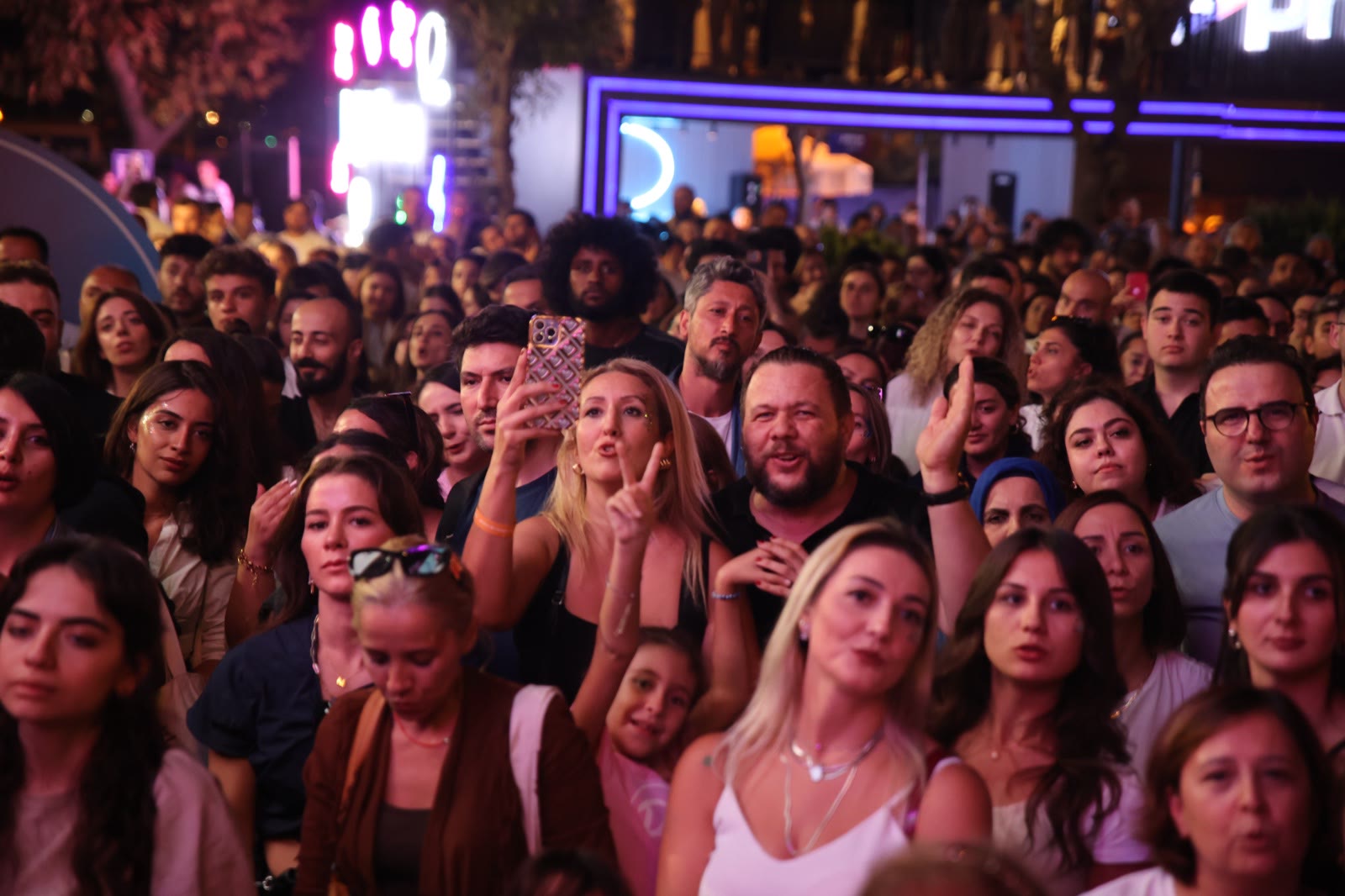 Faces in the night crowd under purple light, phones raised